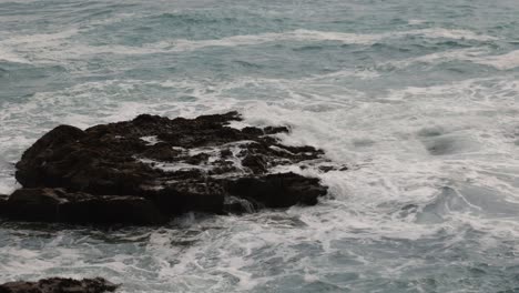 slow-motion-shot-of-waves-crashing-against-rocks-off-of-Fistral-Beach,-Newquay