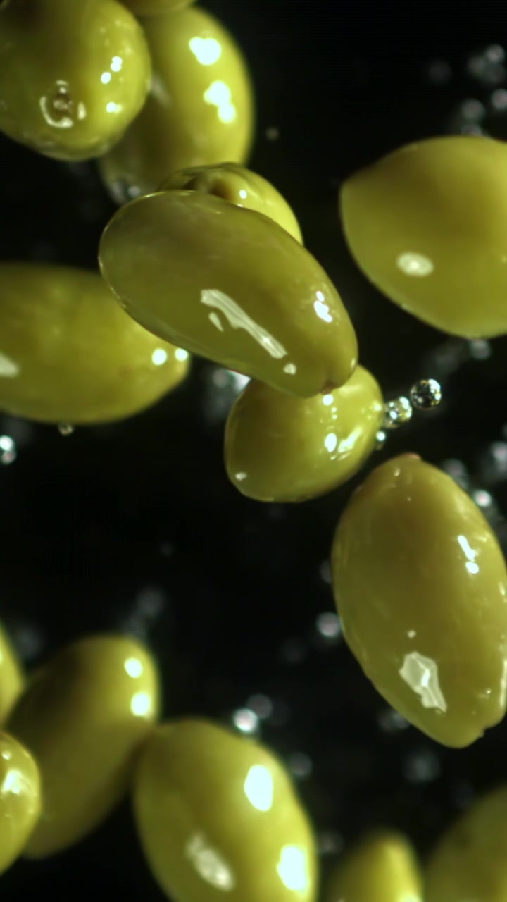 Olive verdi che cadono al rallentatore con gocce d'acqua