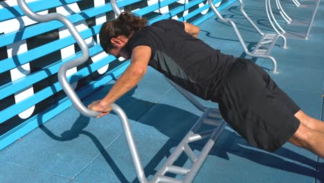 hispanic man does wide grip incline push ups at outdoor gym, medium shot