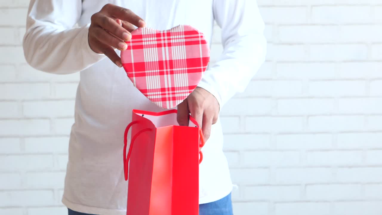 남자가 빨간 가방에서 심장 모양의 선물을 열고