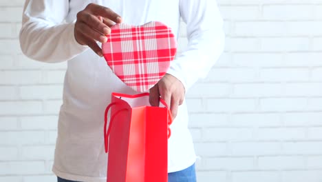 man opening a heart-shaped gift from a red bag