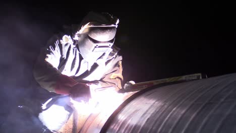 Man-welding-pipeline-at-night-construction