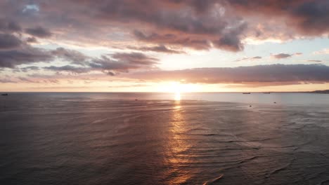 Wide-aerial-shot-of-the-sun-setting-over-the-ocean-horizon-off-the-coast-of-O'ahu,-Hawaii