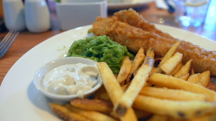 British fish n chips with crispy fish and chips with mushy peas on a table, with a side of tartar sauce