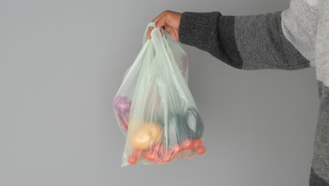 a hand holding a plastic bag full of vegetables