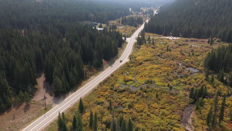 vista aérea de un camión solitario en la carretera en el valle del campo rural en colores otoñales rodeado de bosques de coníferas verdes, disparo de drones