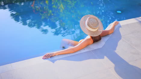 Mujer-Sexy-Sentada-En-El-Borde-De-La-Piscina-De-Un-Hotel-Exótico-Con-Sombrero-De-Paja