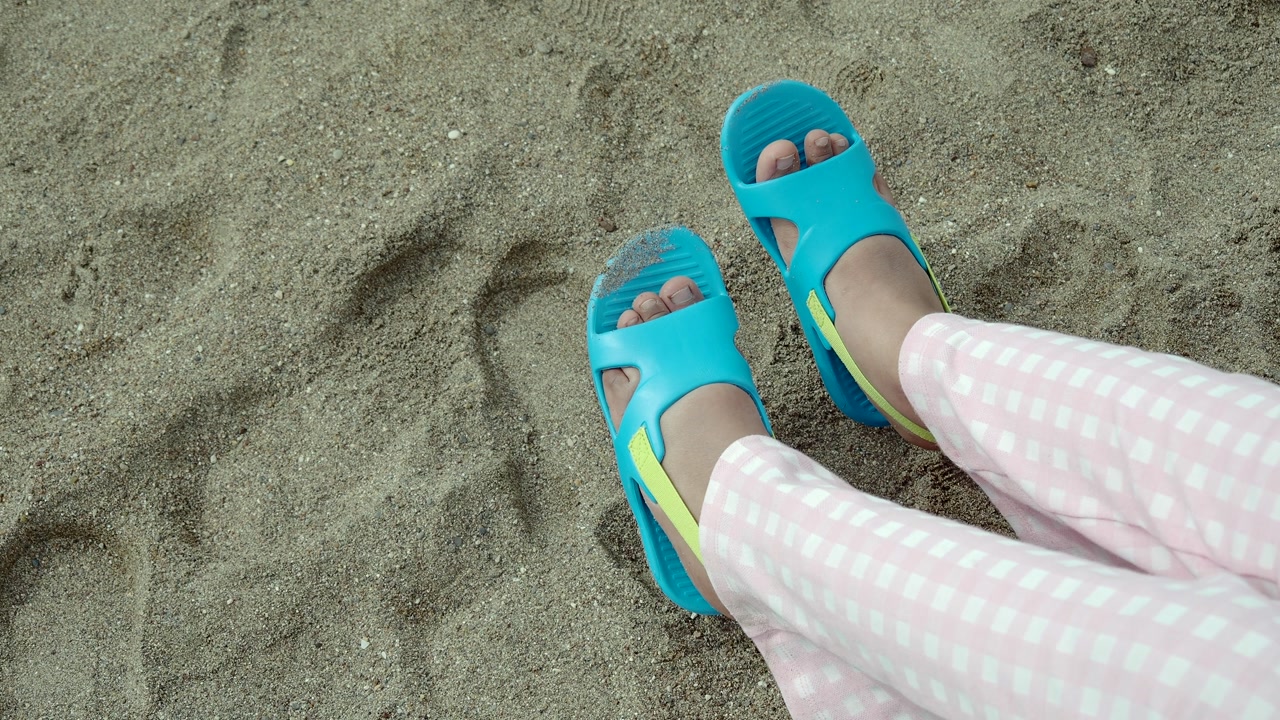 Child's Feet in Blue Sandals Relaxing on Sandy Ground