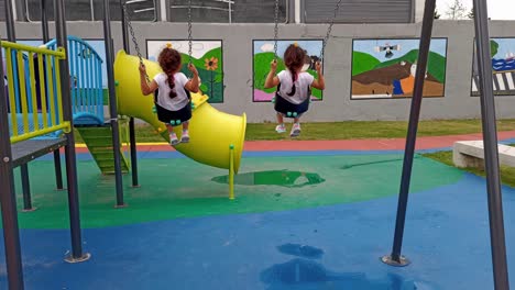 twin girls playing with swing chairs in park