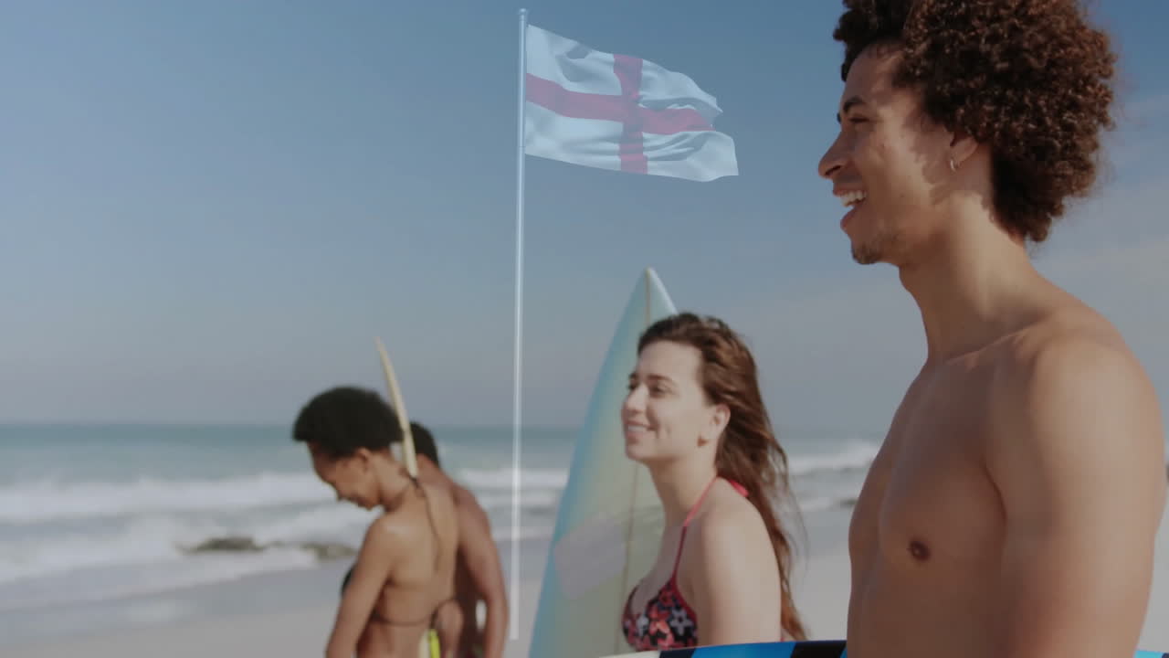 Walking on beach with surfboards, young people near flag waving in background
