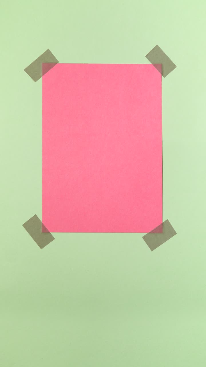 Pink paper note appears and is taped to a pastel green background in a portrait stop motion loop with copy space