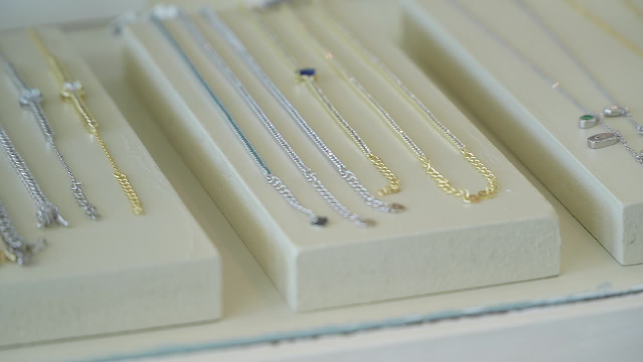 Delicate chains and elegant bracelets of gold and silver are carefully arranged in a glass display case, showcasing their shiny designs under bright sunlight