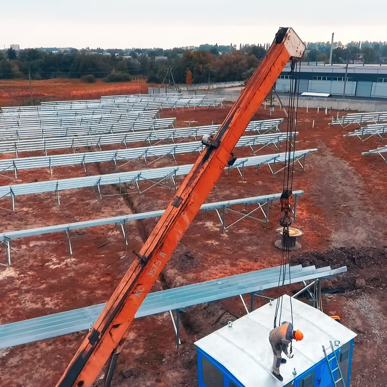 Construction site with installed metal constructions on the field. Male worker standing on top of the booth tries to attach machine hooks