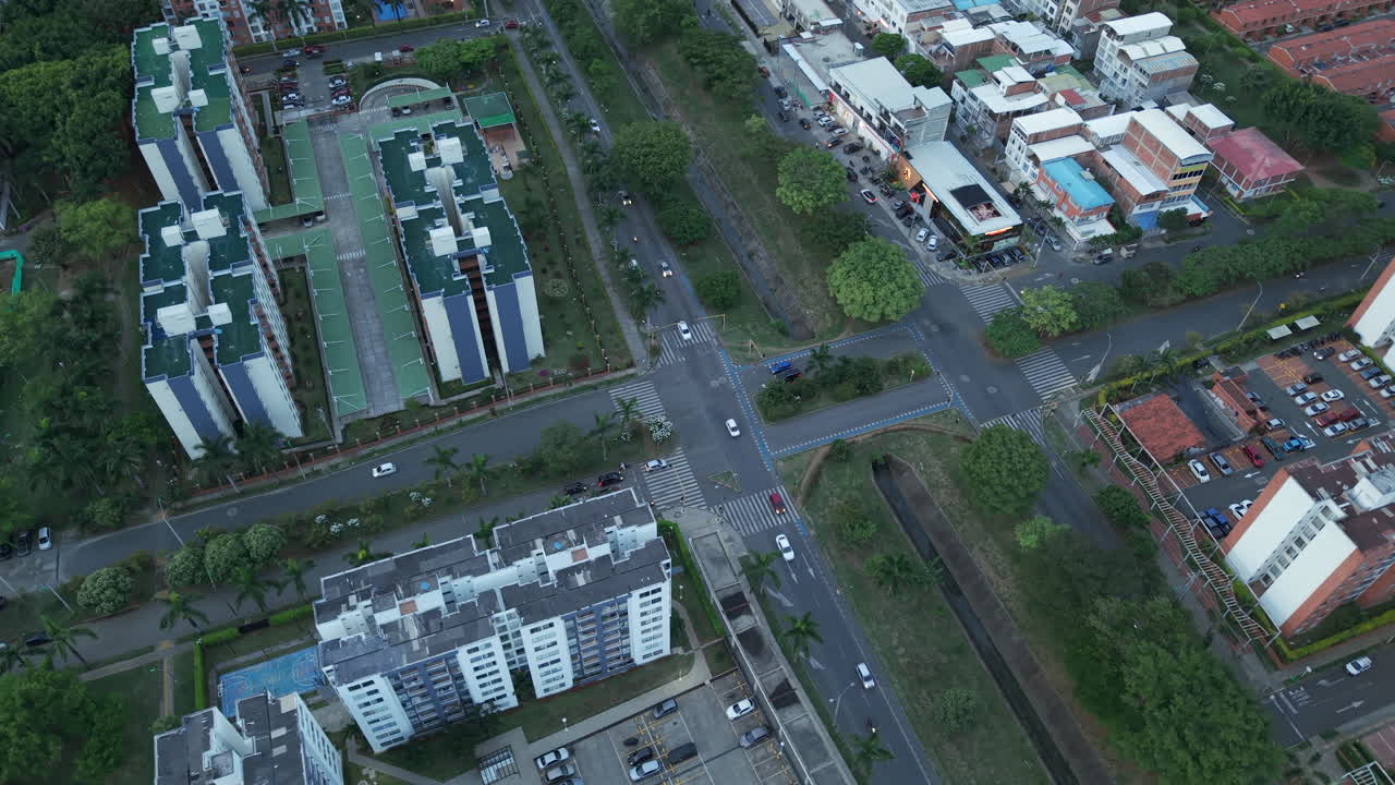 Drone footage captures Valle del Lili in Cali with a panoramic view of buildings, streets, and greenery. The evening light enhances the urban landscape's serene atmosphere