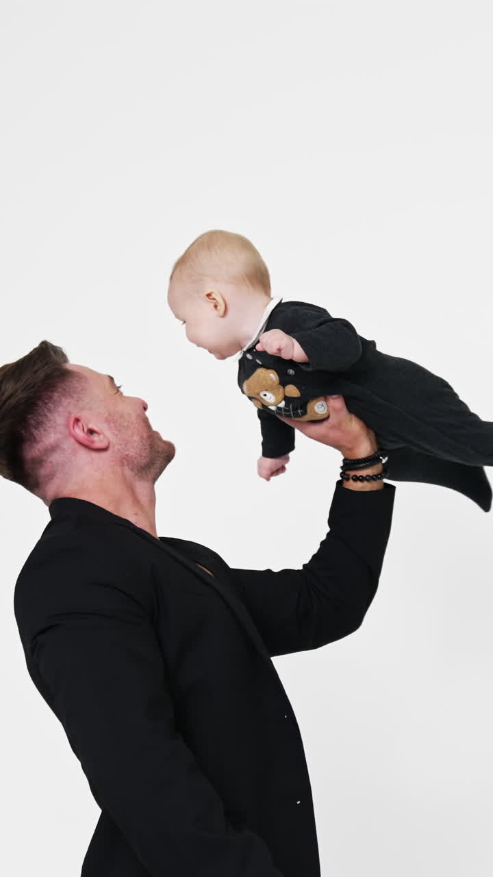 Stilig kaukasisk man i svart jacka med sin lilla baby. Pappan lyfter sitt barn med en hand. Vit bakgrund. Stående video