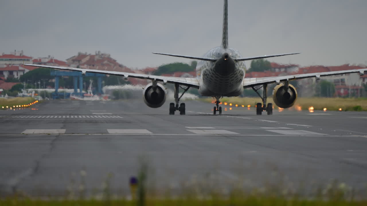 Airplane positioned on runway, ready for takeoff, with cloudy sky and airport structures visible in the background, showcasing aviation activity