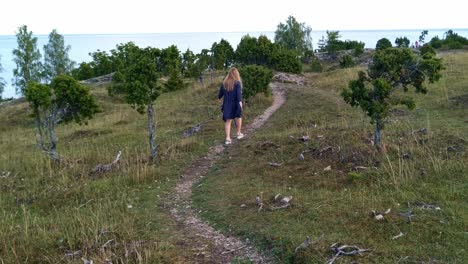 Static-view-of-a-woman-in-a-blue-cardigan-walking-along-a-path-in-nature-and-waving-her-arms-in-a-little-dance-in-Uugu-Nature-Park,-Estonia