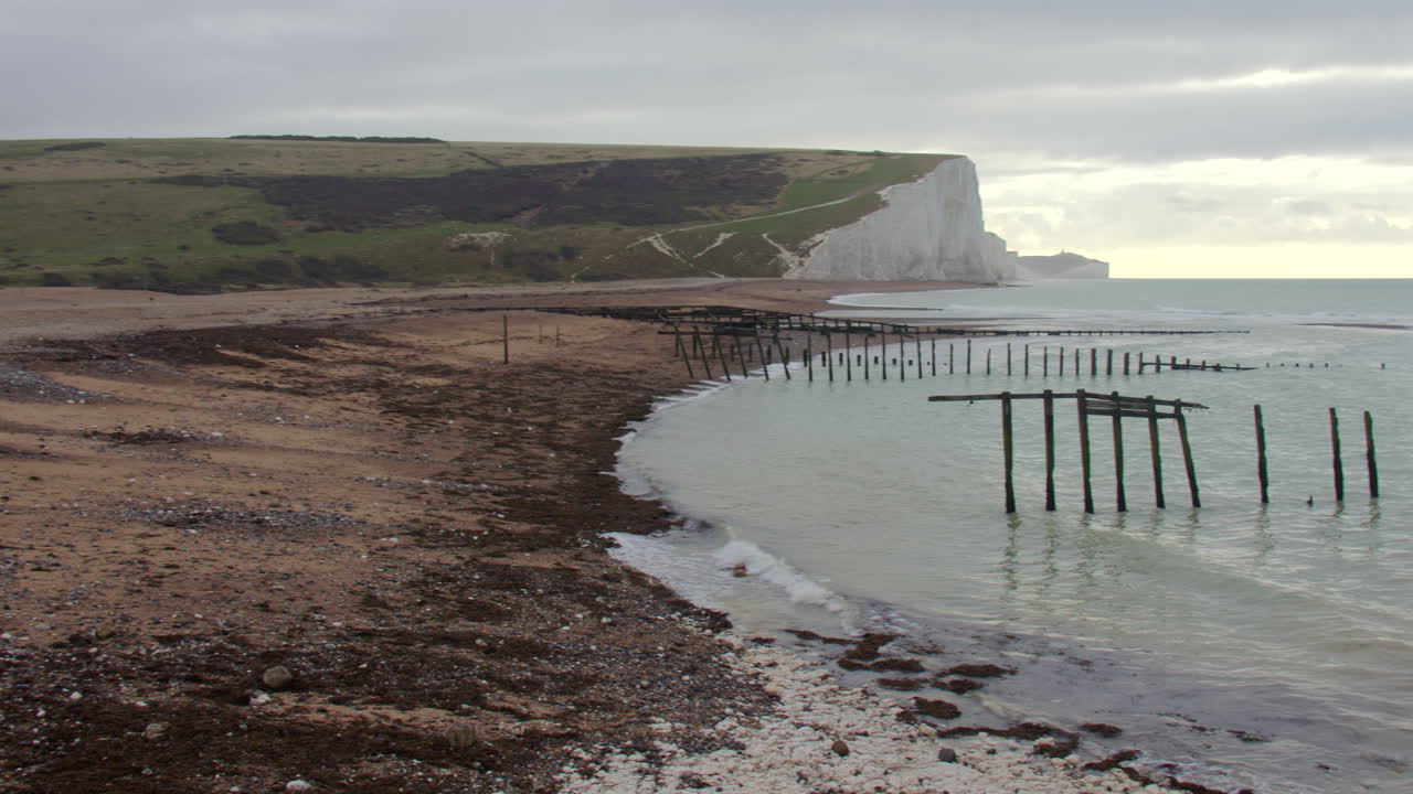 Panoramica extra larga da sinistra a destra delle scogliere di Seven Sisters dalla spiaggia con frangiflutti rotti a Cuckmere Haven, vicino a Seaford Head