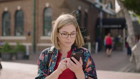 portrait of young blonde woman texting browsing using smartphone social media app wearing glasses in urban background