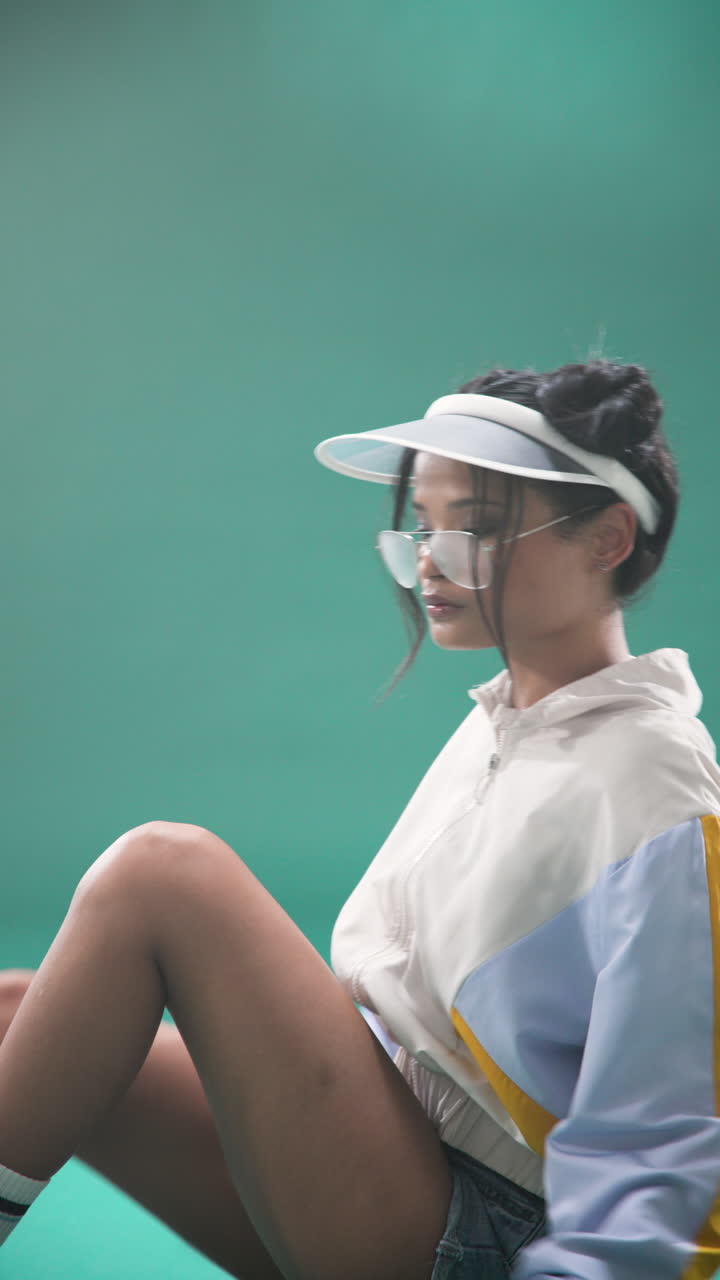 Vertical video: Young woman in retro sportswear posing confidently against green background