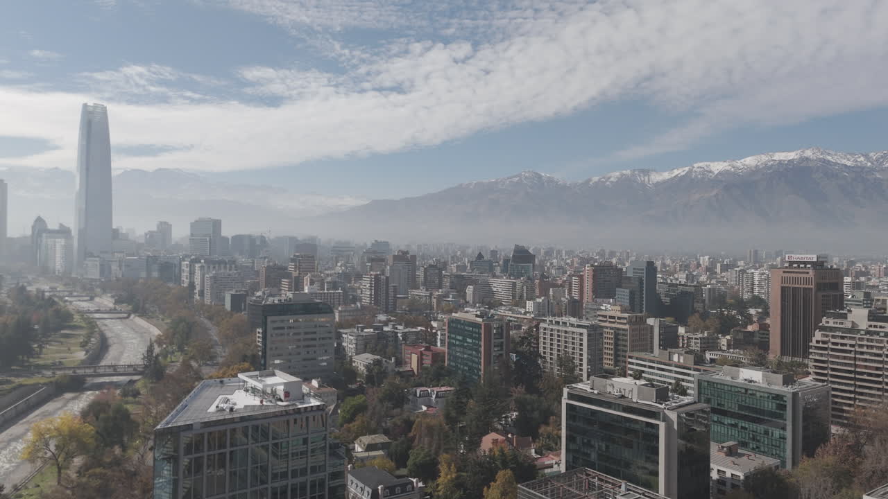 Sideways drone shot of Santiago de Chile in South America watching over the skyscrapers and big buildings with snowy mountains in the background on bright but cloudy day LOG