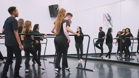 male and female students at performing arts school rehearsing ballet in dance studio using barre