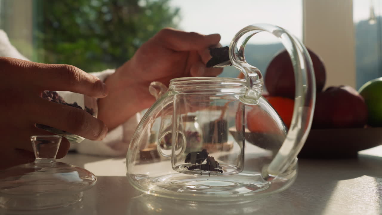 hombre transfiere el té a la tetera con cuchara. joven arregla accesorios de té preparando el escenario para una ceremonia sincera. desayuno saludable por la ventana