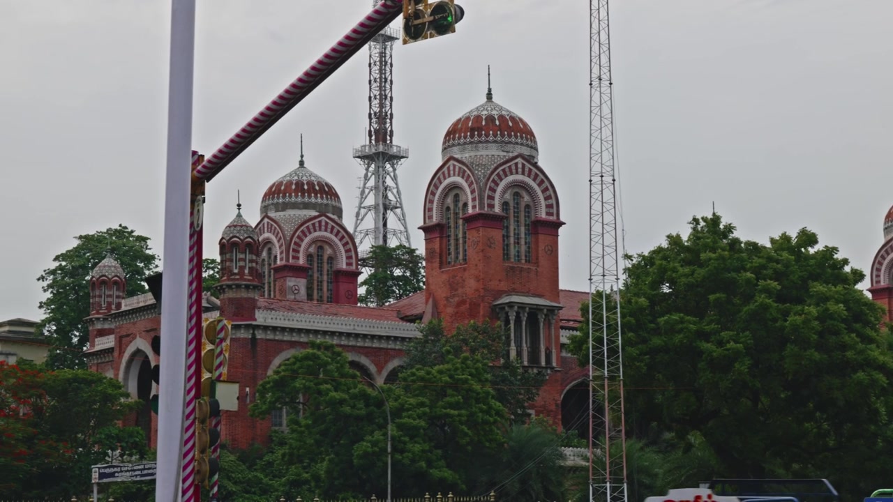 Edificio dell'Istituto di Educazione a Distanza con alberi e un palo del semaforo sulla strada costiera, Triplicane, Chennai, Tamil Nadu, India. Di sera, panoramica, 4K.