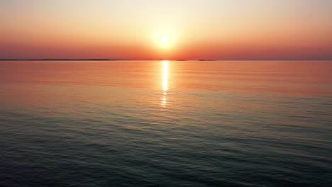 Aerial-Drone-View-of-Gorgeous-Ocean-Sunset-with-Bright-Glowing-Sun-Casting-Colorful-Red,-Orange,-Purple-and-Yellow-Reflections-Over-Peaceful-Rippling-Waves-of-the-Sea-with-Beautiful-Sky-and-Water