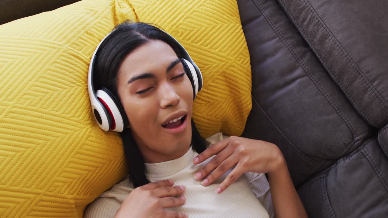 género fluido hombre con auriculares disfrutando de escuchar música mientras está acostado en el sofá en casa