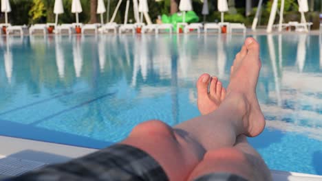 Men's-feet-on-the-background-of-the-swimming-pool,-relax-on-vacation