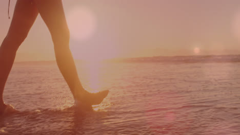 Animation-of-lights-over-legs-of-caucasian-woman-walking-on-beach