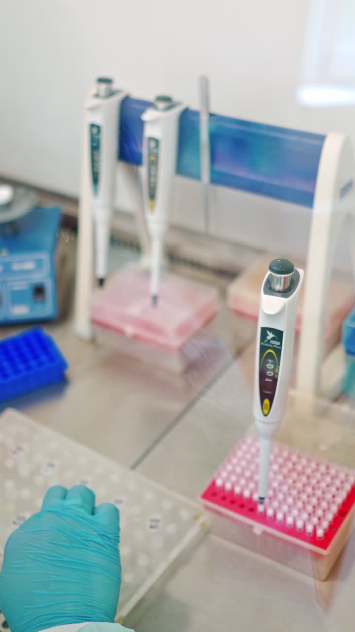Close-up work of medical scientist with test tubes on sterile table. Hands in protective gloves of female assistant working with plastic vials in the laboratory. Vertical video