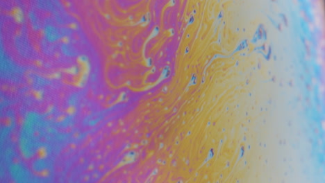 macro shot of small cells moving on a viscous rainbow colored liquid to the right side of the frame to a bright spot