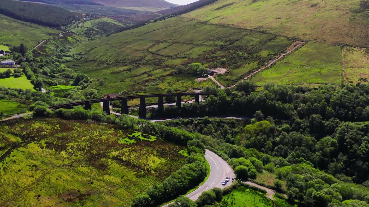 Luftfoto som sirkler rundt Gleensk viaduktbro omgitt av skog med en svingete vei og biler som krysser en enveiskjørt landlig bro