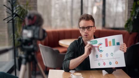 stylish young man with glasses makes a presentation on slides infographics and records video on camera on a tripod