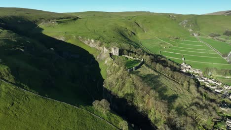 Rising-aerial-sunrise-establishing-shot-of-Peveril-Castle,-located-in-the-Peak-District-town-of-Castleton,-UK