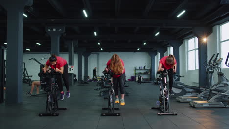 group athletic girls performing aerobic riding training exercises on cycling stationary bike in gym