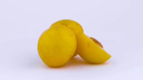 two whole and one half cut of a big yellow mirabelle plums with the pit. slowly rotating on the turntable isolated on the white background. close-up