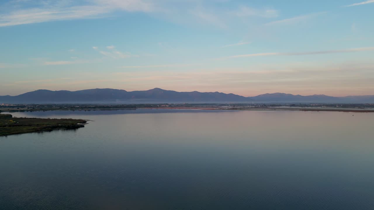 Aerial: Sideway drone flight during sunrise along coastline with mountain backdrop