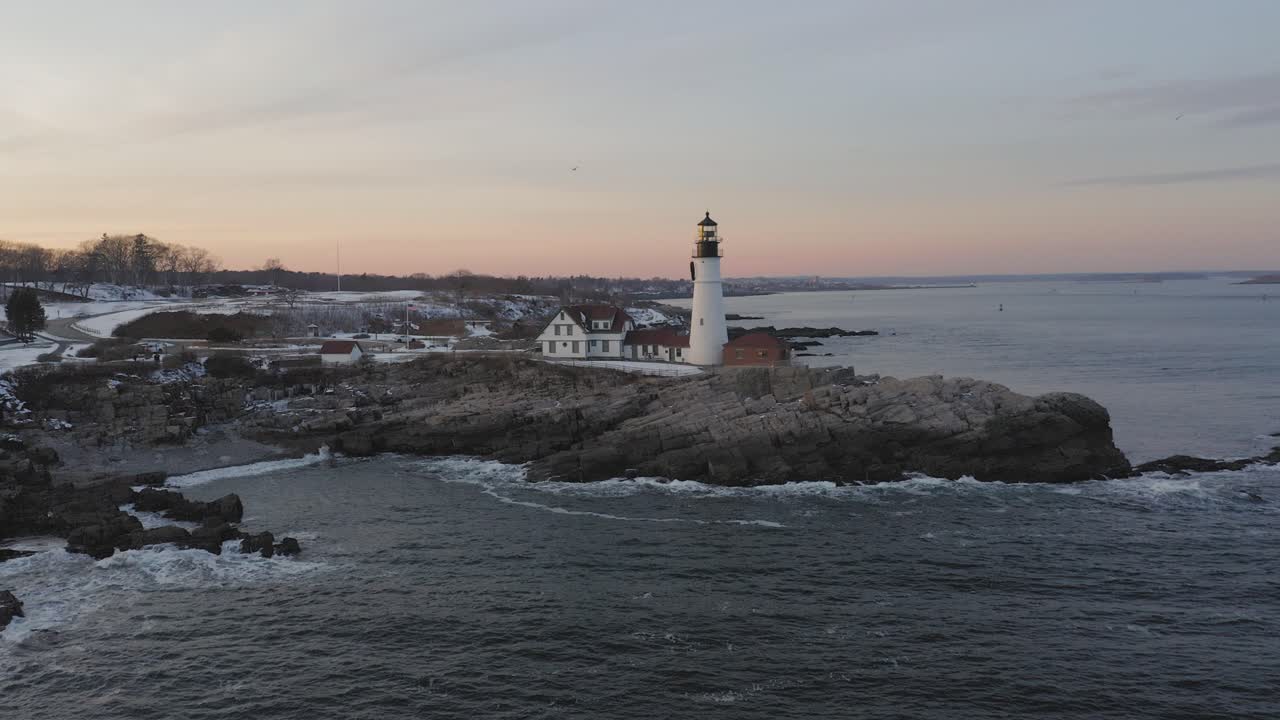 Hidas ilmakuva kiertäen Cape Elizabethin majakkaa talvisen auringonlaskun aikaan.