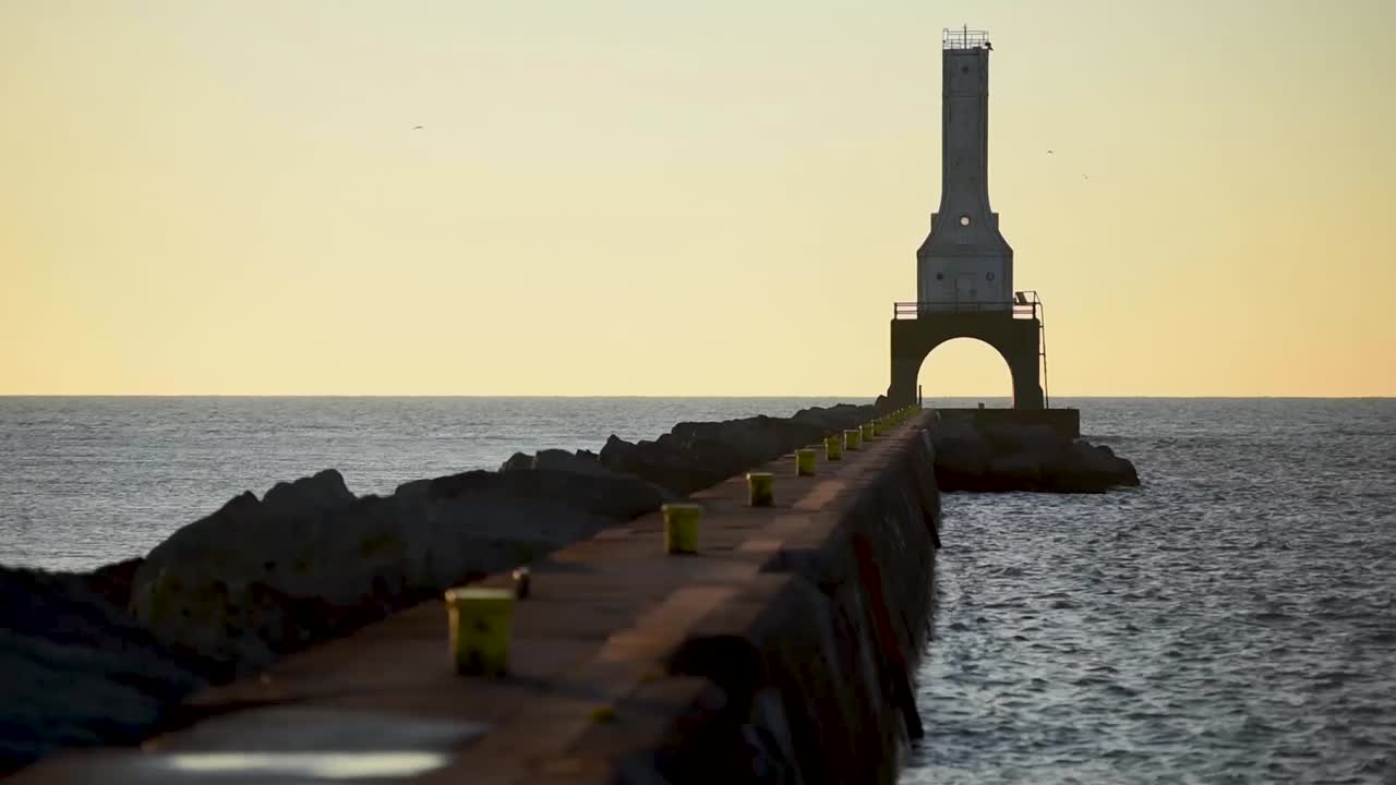 los pájaros vuelan, las aguas del lago michigan brillan en el puerto deportivo mientras la luz del sol de la mañana besa el mar mientras el rompeolas lleva el camino al faro del puerto de washington wisconsin