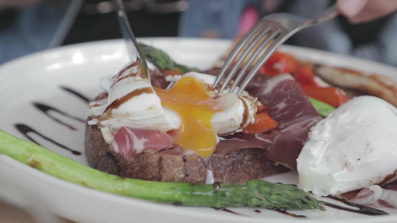 Poached egg gets cut by a knife and the yolk oozes out in slow motion.