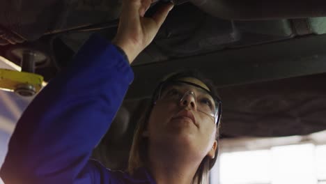 Mecánica-Femenina-Con-Gafas-Protectoras-Inspeccionando-Un-Automóvil-En-Una-Estación-De-Servicio-De-Automóviles