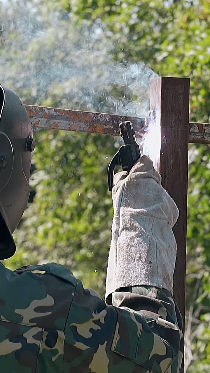 slow motion backside view builder in mask welds upper parts of fence carcass with modern instrument