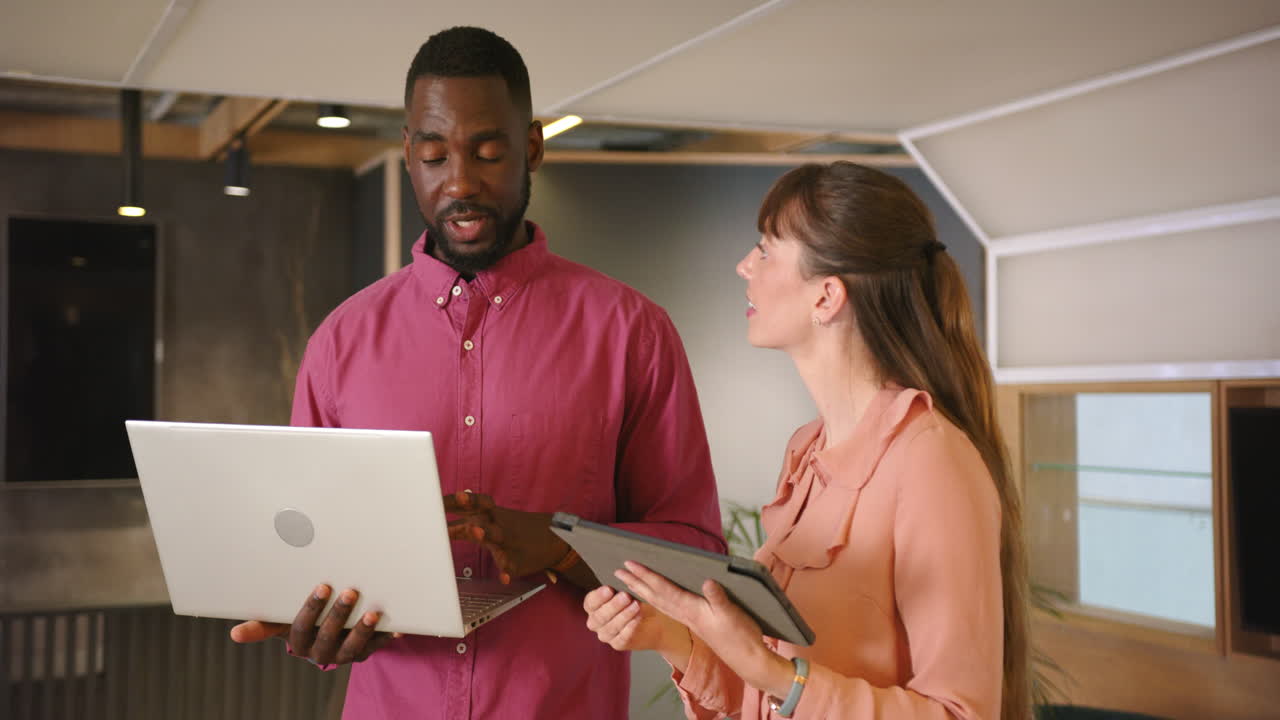Discussing project details, diverse colleagues using laptop and tablet in modern office