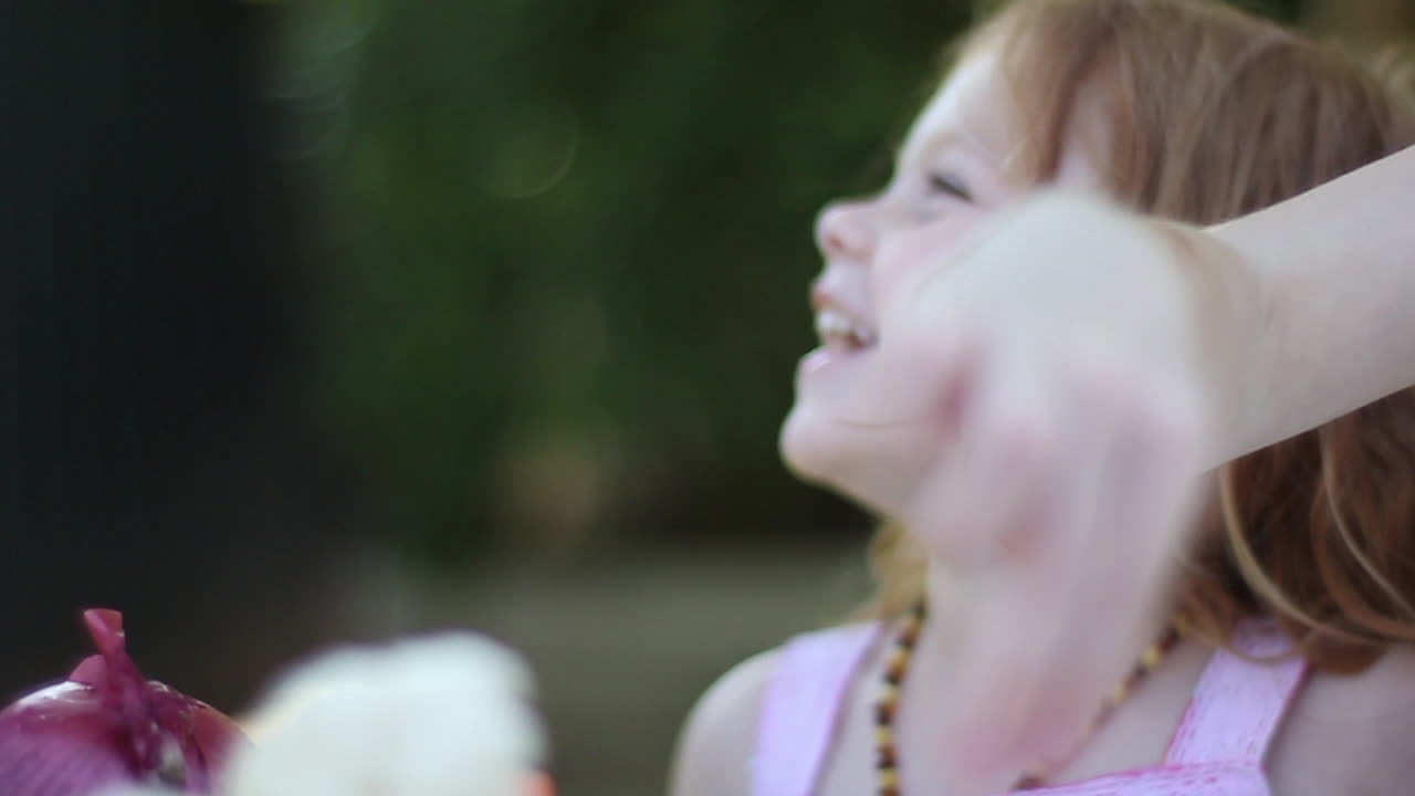una niña en edad preescolar con cara sonriente mirando a su padre fuera de la pantalla en un picnic en el patio trasero