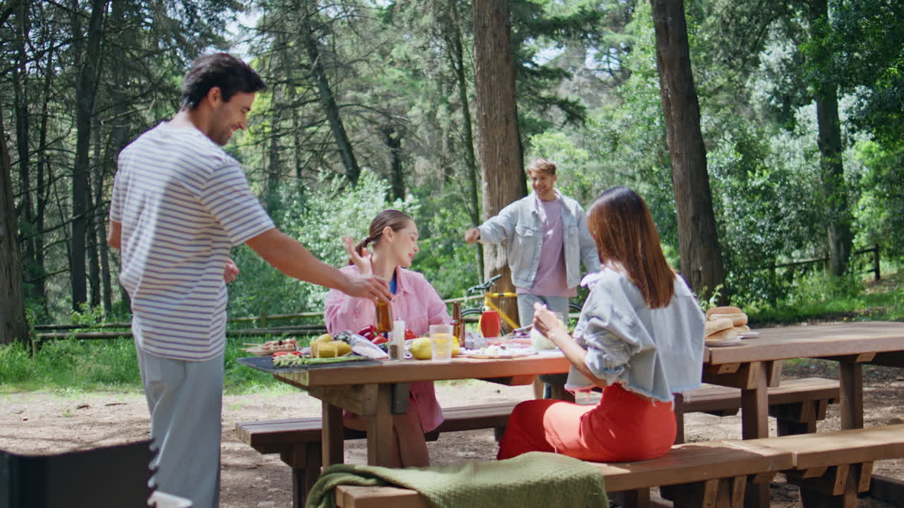Carefree friends spending picnic in forest. Smiling people greeting
