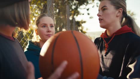 Close-up-three-blonde-girls-in-sportswear-communicate-with-each-other-with-a-basketball-and-stand-on-a-street-court-on-a-sunny-day-in-summer