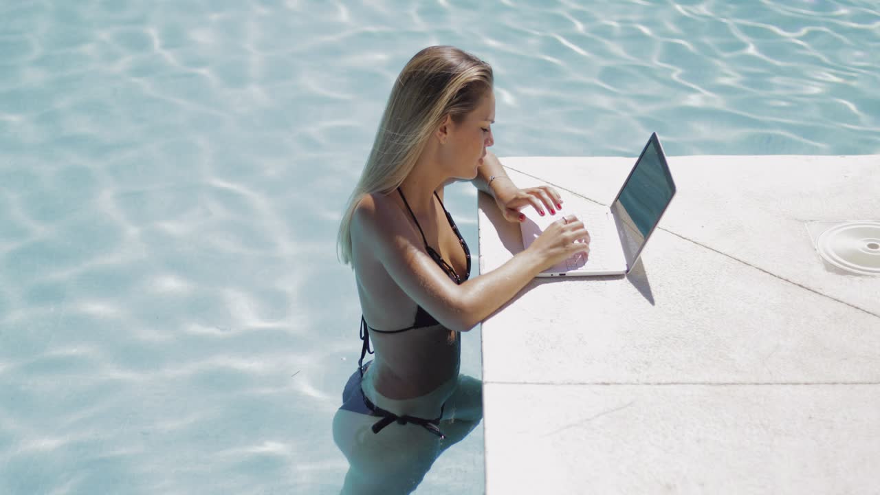 девушка отдыхает в бассейне и пользуется ноутбуком